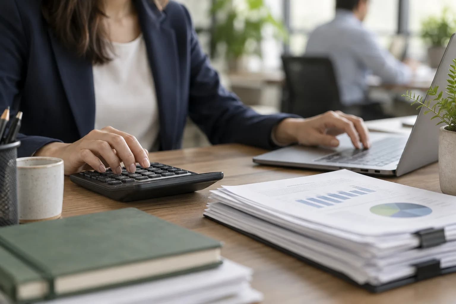 Hands working a calculator and keyboard beside printed payroll reports